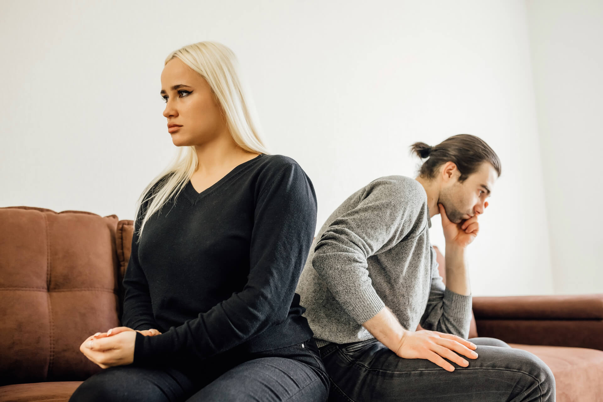 A couple sits back-to-back on a couch, looking away from each other with tense expressions, symbolizing marital conflict and the need for an affordable divorce lawyer in Irvine.