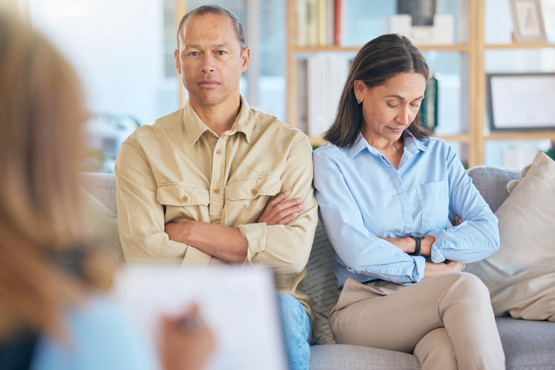 A couple sits with arms crossed on a couch during a legal consultation, reflecting tension and the need for guidance from a divorce attorney in San Clemente.