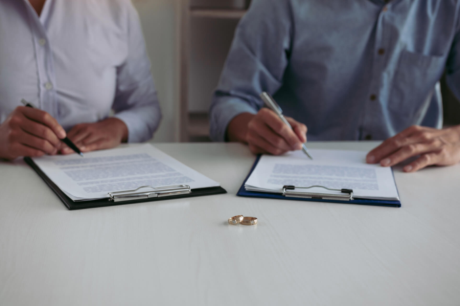 A couple sits at a table signing divorce documents with their wedding rings placed between them, symbolizing the finalization of their marriage with the help of a divorce lawyer in San Diego.