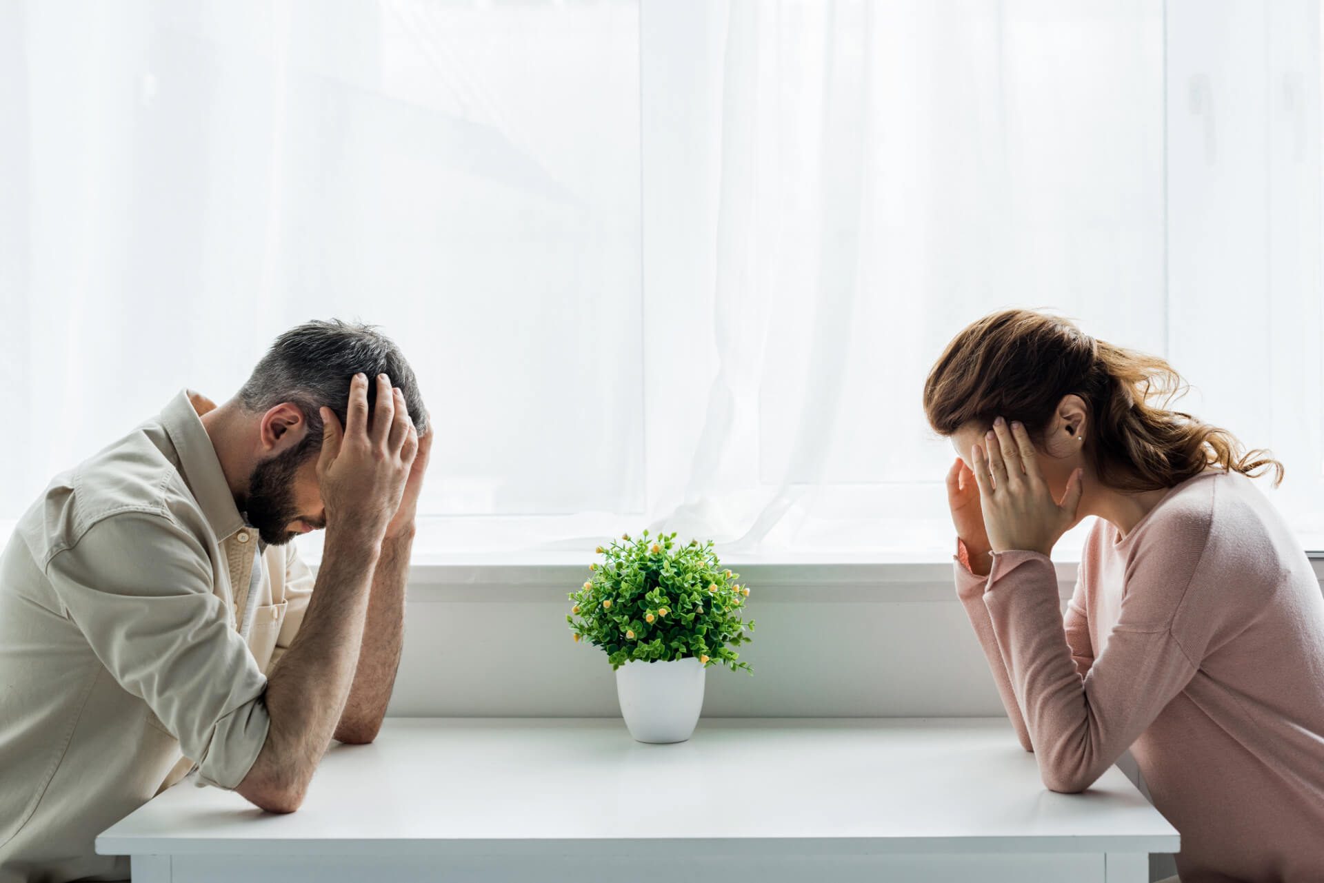 A distressed couple sits across from each other at a table, heads in their hands, symbolizing the emotional strain of divorce and the need for a Laguna Beach divorce lawyer.