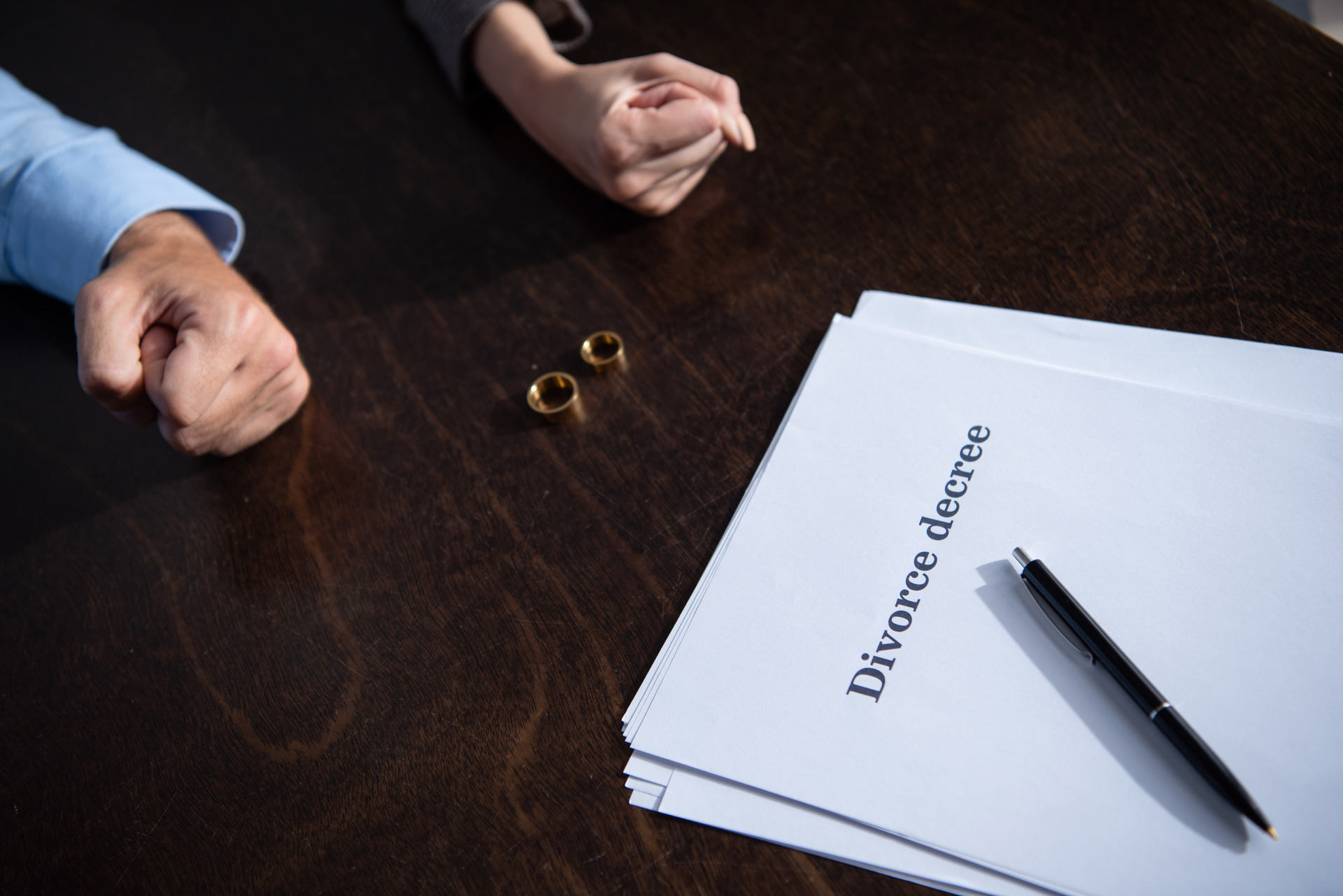 Divorce-decree-and-wedding-rings-on-a-table-with-a-tense-couple-showing-clenched-fists-in-the-background.-Mission-Viejo-Divorce-Lawyer-offering-legal-support-for-divorce-settlements